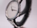 Angled side view of the Michael Kors watch, showing the polished silver-tone case and the signed 'MK' crown.