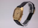 Side angled view of the Certina Newport watch, showing the gold case and crown, on a display stand.