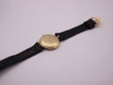 View of the watch from the back, showing the gold case back and the full black leather strap with buckle.