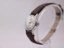 Angled side view of the Seiko watch, showing the crown and slender case profile on a watch stand.