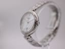 Side view of the Tissot watch showing the polished stainless steel case and fluted crown on a clear display stand.