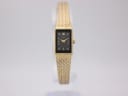 Front view of the gold-tone Rotary ladies watch with a black rectangular dial on a clear stand.