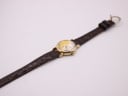 Top-down view of the watch and full length of the brown leather strap with gold-tone buckle on a white background.