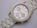 Close-up, angled view of the Michael Kors white chronograph dial with gold-tone details and the white ceramic bracelet extending away.