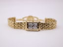 Full front view of the gold Raymond Weil Tango watch with its integrated bracelet laid flat on a light background.