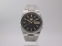 Front view of the Seiko 7009-3130 watch with black dial and gold baton indices on a stand.