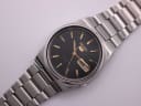 Top-down view of the Seiko 7009-3130 watch with black dial, day-date display, and stainless steel bracelet.