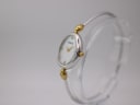 Angled side view of the Michel Herbelin watch on a clear stand, showing the oval case and integrated two-tone bangle.