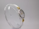 Another angled side view of the watch on its stand, highlighting the jewellery-like bangle design and gold-tone crown.