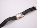 Full view of the Gucci watch from an angle, highlighting the black leather strap and the gold-tone buckle.
