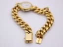 Close-up of the gold-tone fold-over clasp of the watch bracelet, open and ready to fasten.