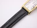 Detail shot of the black textured leather strap and lug area of the gold-plated watch case.
