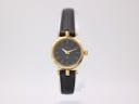 Front view of the vintage Gucci 2000L ladies watch on a clear stand, showcasing its black dial with gold roman numerals and gold-toned case.
