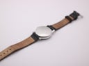 Rear view of the Mondaine watch laid flat, showing the case back and the interior of the black leather strap.