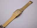 Top-down, slightly angled view of the complete gold-tone Seiko watch with its integrated metal bracelet extended.
