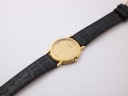Top-down view of the Favre-Leuba watch with gold case and black leather strap stretched out.
