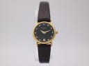 Front view of a gold Raymond Weil 9923 ladies' watch with black dial and diamond-effect indices on a clear watch stand.