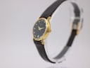 Angled left view of the gold Raymond Weil 9923 watch on a stand, highlighting the case profile and brown leather strap.