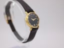Angled right view of the gold Raymond Weil 9923 watch on a stand, showing the crown and elegant case shape.