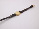 Back view of the Raymond Weil 9923 watch laid flat, revealing the gold case back and the full brown leather strap with buckle.