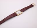 Overhead view of the Raymond Weil watch with brown leather strap extended, showing the gold buckle.