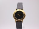 Front view of the gold-plated Gucci 3000.2.L quartz watch with a black dial and roman numeral bezel on a white stand.