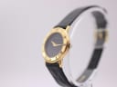 Angled side view of the Gucci watch on a stand, highlighting the gold-plated case and crown detail.