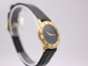 Angled view of the Gucci watch from the left, showing the gold bezel with roman numerals and black leather strap.