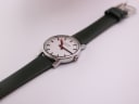 Top-down angled view of the Mondaine watch with the green leather strap extended.