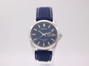 Front view of the Seiko V743-9A20 watch, silver case, blue dial with day-date, and navy rubber strap, on a clear stand.