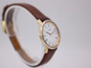 Another angled side view of the watch, showcasing the contrasting metals of the case and the brown leather strap on a display stand.