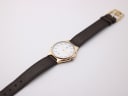 Overhead angled view of the entire Yves Saint Laurent watch, displaying the brown leather strap and two-tone case.