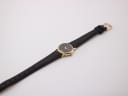 Overhead view of the Raymond Weil 9923 watch with its black leather strap extended, showing the gold-tone buckle.