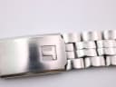 Close-up of the stainless steel bracelet's fold-over clasp with an embossed Tissot 'T' logo and visible surface scratches.