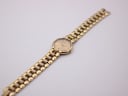 Top-down full view of the Christian Dior gold-tone watch with its integrated bracelet extended against a white background.