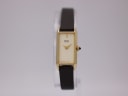 Front view of the gold-tone rectangular Seiko watch with cream dial and brown leather strap on a watch stand.