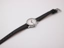 Overhead shot of the Mondaine watch, extended on its black leather strap, showing the full length against a white background.