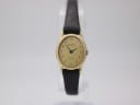 Front view of the Raymond Weil 5717 watch, showing the round gold-toned case, champagne dial with black numerals, and black lizard-grain leather strap on a clear stand.
