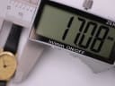 Digital caliper display showing an exact measurement of 17.08mm, with the Raymond Weil watch blurred in the background, confirming its case size.