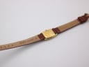Rear view of the watch showing the gold-plated case back and the underside of the brown leather strap with "GENUINE LEATHER" and "12" mark.