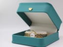 The gold-tone Raymond Weil watch displayed in a green presentation box with a gold crown emblem.