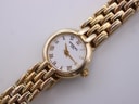 Top-down view of the Raymond Weil watch with its white dial, black Roman numerals, and gold-tone hands.