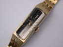 Close-up of the Seiko watch dial, displaying the gold baton indices, dauphine hands, and vertically textured two-tone design.