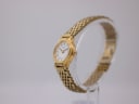 Angled side view of the gold-tone Seiko watch on a clear stand, showing the curved case and multi-link bracelet.