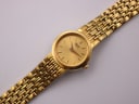 Top-down view of the Seiko watch and its full gold tone stainless steel bracelet on a white surface.