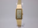 Front view of rectangular gold plated Seiko 1320-5780 quartz watch with cream dial on a clear stand.