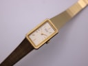 Close-up diagonal view of the cream dial with minimalist gold baton indices and slender hands.