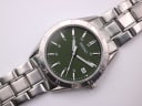 Top-down close-up of the Seiko green dial, luminous hands, date window, and steel bracelet links.