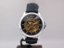 Front view of generic skeleton automatic watch with a black dial and gold-tone movement on a stand.