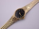 Close-up of the black oval dial of the gold tone Citizen watch, featuring minimal text and gold-tone hands.